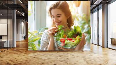 Joyful woman savoring a delicious salad at home during the day, bathed in natural daylight, highlighting a relaxed and healthy lifestyle. Wall mural