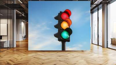 Traffic light with red, amber, and green lights illuminated under bright sunlight, set against a clear blue sky with clouds Wall mural