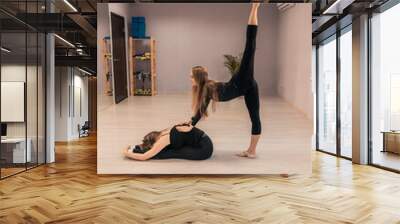 Beautiful young woman is engaged in gymnastics in the gym. The athletic body of the girl is covered with tight-fitting yoga clothes. Wall mural