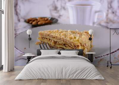 A portion of almond cake in a ceramic plate on the table next to cup of tea Wall mural