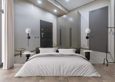 Modern design of the hallway, decorated in light beige color. Black front door, .grey wardrobe. Wall mural