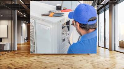 a professional electrician man is fixing a heavy duty unit of central air conditioning system by his tools on the roof top and wearing  uniform and white cap Wall mural