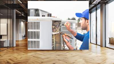 a professional electrician man is fixing the heavy unit of an air conditioner at the roof top of a building and wearing blue uniform and head cap Wall mural