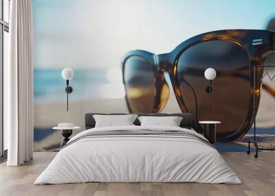 Sunglasses resting on sandy beach with ocean in background. Wall mural