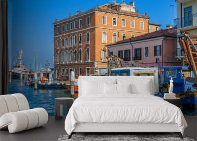 Boats and fishing industrial ships moored in water canal and old buildings on embankment in Chioggia town historical centre, blue sky background in summer day, Veneto Region, Northern Italy Wall mural