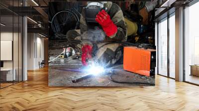 A male welder in a welding mask works with an arc electrode in his garage. Welding, construction, metal work. Wall mural