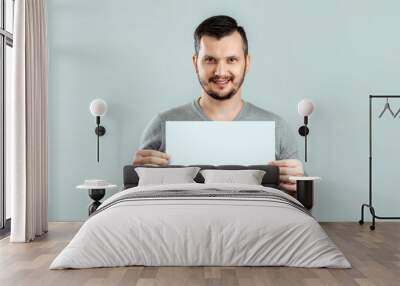 A young, attractive man holding a blank white A4 sheet, on a light background. mockup, layout, copy space. Wall mural