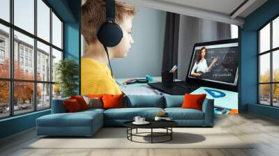 Distance learning, a boy in headphones sits at a table at home looking in a beech laptop. The concept of online education, home education, technology, school. Wall mural