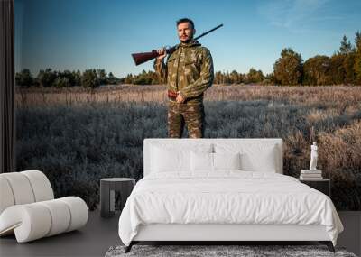 Hunter man in camouflage with a gun during the hunt in search of wild birds or game on the background of the autumn forest. Autumn hunting season. The concept of a hobby, killing. Wall mural