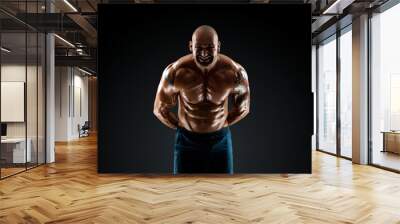 Male bodybuilder with light stubble with a naked torso posing against a dark background. The concept of a fitness club, doing sports, weightlifting. Copy space. Wall mural