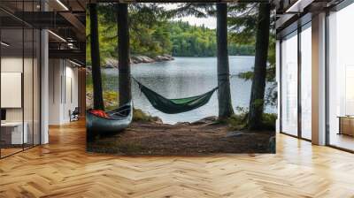 A tranquil lakeside camping setup with a hammock between two trees and a canoe nearby Wall mural