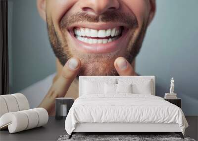 Man smiles broadly and shows off snow-white healthy teeth after going to dentist. Happy guy pointing fingers at mouth recommends good toothpaste for beaming smile Wall mural