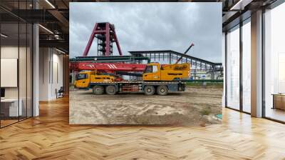 A large yellow truck crane stands ready to work on the construction site of the new plant Wall mural