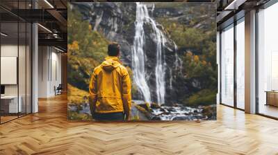 A back view of man wearing a yellow hoodie jacket on waterfall nature background. Wall mural