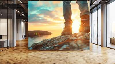 A person is standing on a rocky cliff overlooking the ocean. The sky is a mix of blue and orange, creating a serene and peaceful atmosphere Wall mural