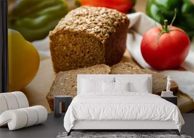 Sliced loaf of black rye bread with sunflower seeds, along with tomatoes and peppers. Bread and vegetables on a wooden table. Wall mural