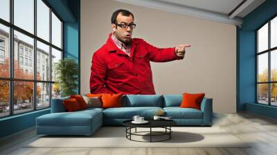 Surprised man in red jacket pointing to the side with exaggerated expression for a quirky and humorous portrait concept featuring bold fashion and playful personality in a minimalist studio setting Wall mural