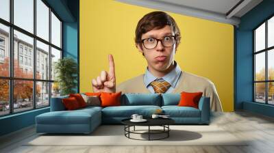 Young man in casual attire making expressive face with finger raised against vibrant yellow background Wall mural