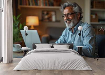 Mature eastern Indian man sitting at home desk front of laptop greeting business partner on screen. 40s freelance entrepreneur businessman communicate remotely online with colleague using pc computer Wall mural