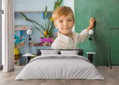 A little cute boy at school is standing near the blackboard and writing on it. Back to school concept Wall mural