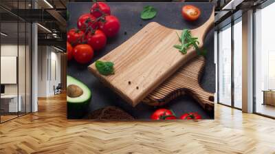 wooden chopping board with tomatoes, avocado, arugula on a dark background Wall mural