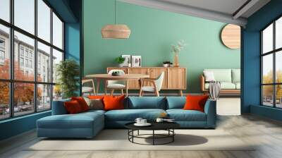 Mint color chairs at round wooden dining table in room with sofa and cabinet near green wall. Scandinavian, mid-century home interior design of modern living room Wall mural