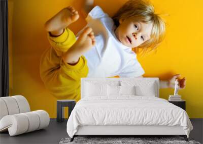 The kid is 2 years old with blonde hair, dressed in a white T-shirt and yellow pants on a yellow background. Emotions. The concept of childhood and family. Baby front view yellow isolated background Wall mural