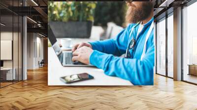 image of young bearded man sitting in a cafe with cup of coffee, using pc at the table - business ma Wall mural