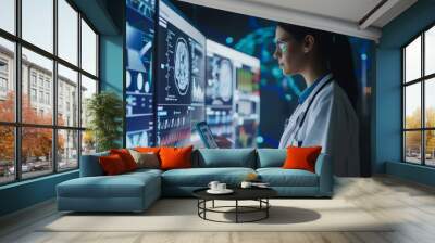 A woman in a white lab coat is looking at a computer screen with a tablet in her hand. She is looking at a graph of a patient's health data Wall mural