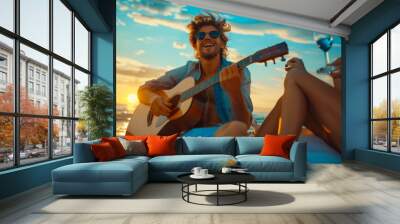 Group of happy friends having fun outdoors. A young man sits on the beach at sunset and plays the guitar. Lifestyle. Vacation concept. Wall mural