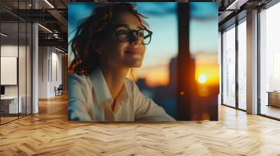 Young woman with glasses smiles while using a laptop at night surrounded by glowing warm lights Wall mural