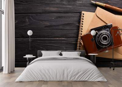 An envelope, a beautiful camera and a notebook with a pen on a black wooden background with a place for an inscription Wall mural