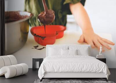 The child pours chocolate dough into a red silicone mold on a white table. Making a Christmas cookie. Wall mural