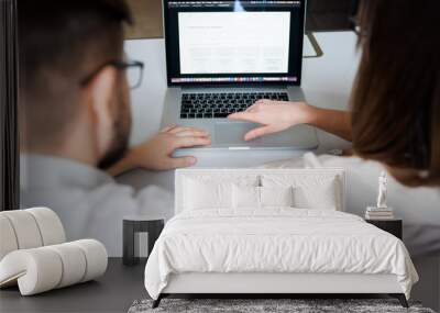 Two young coworkers dressed casual using laptop in white interior Wall mural