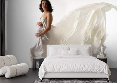 Happy woman waiting for a baby, wrapped in flowing white silk on a white background. The concept of femininity, happiness, fashion, motherhood. Wall mural