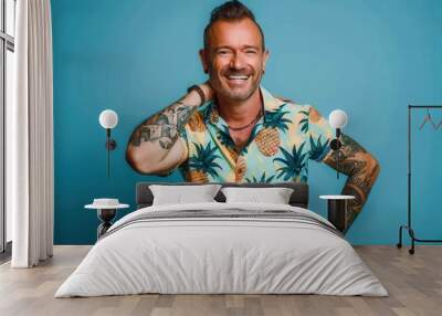 Vibrant Portrait Portrait of a mid-age man with tattoos wearing a pineapple printed shirt smiling and looking at the camera. He is standing in front of a blue studio background. Wall mural