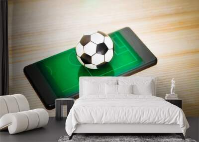 A toy soccer ball on a smartphone with a picture of a green field. Concept of the game of football. Wall mural