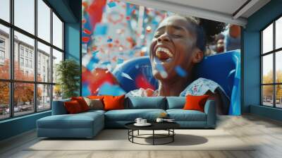 Young African American girl screaming and cheering on a rollercoaster in amusement park. Blue and red confetti falling around. July 4th independence day USA celebrations in summer. Patriotic american. Wall mural