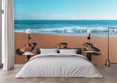 Footprints in the sand near gentle waves on a serene beach during a clear sunny day Wall mural