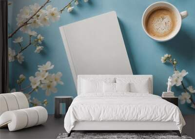 Blank book cover template laying on blue background with a cup of coffee and spring flower branch. Front, top view of empty book mockup in cosy environment and pastel colours Wall mural