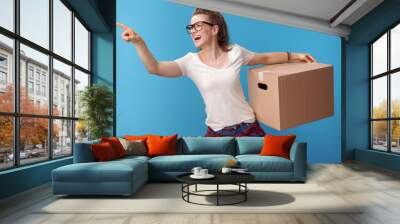 happy woman with cardboard box pointing at something on blue Wall mural