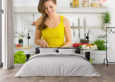 Happy young woman cutting fresh vegetables in kitchen Wall mural