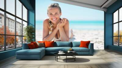 Portrait of smiling young woman laying on beach Wall mural