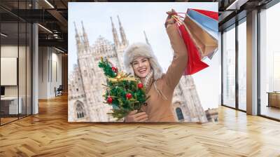 woman with Christmas tree and shopping bags in Milan rejoicing Wall mural