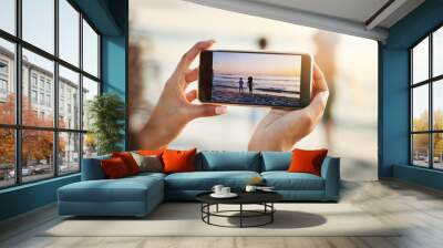 Phone, photograph and beach with a woman in nature, recording her playing kids by the ocean outdoor. Mobile, family and sunset with a parent taking a picture of her kids on the sand at the sea Wall mural