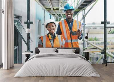 Builder and engineer working together as a construction team on a building site and standing on scaffolding. Portrait of a man and woman in a hardhat and vest at work on a new development project Wall mural