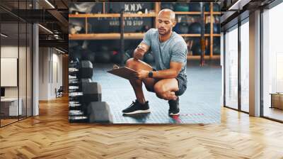 Doing some checks around the centre. Shot of a muscular young man using a clipboard while checking equipment in a gym. Wall mural