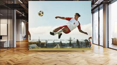 Soccer, game and man kicking a ball during training with the team on a field for sports. Athlete football player in the air to jump for a goal while playing in a professional match or competition Wall mural