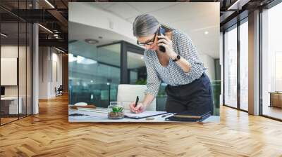 The appointments are filling up. Shot of a confident mature psychologist using a smartphone and making notes in a modern office. Wall mural