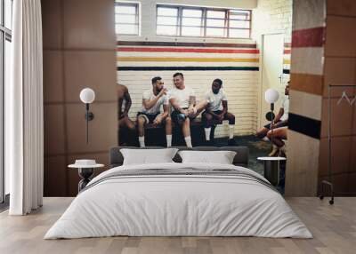 Winner sit here. Full length shot of a group of handsome young rugby players having a chat while sitting together in a locker room. Wall mural